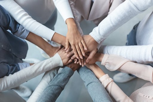 Sieben Personen stehen im kreis und legen in der Mitte die Hände aufeinander. Nur die Arme und Hände sind sichtbar.