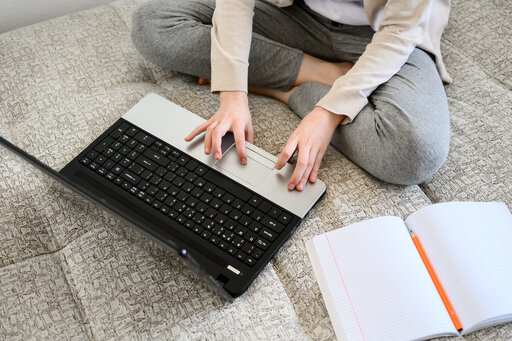 Eine Person sitzt im Schneidersitzt vor einem Laptop und bedient diesen.